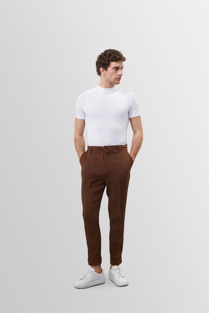 T-shirt blanc slim fit pour homme Frédéric, coupe ajustée et moderne, en tissu doux avec col rond, porté avec un pantalon marron et des baskets blanches pour un look tendance et épuré.