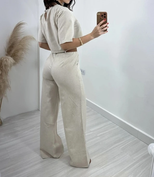 cet ensemble beige composé d'un pantalon évasé et d'un top à manches courtes offre une coupe élégante et décontractée. Le pantalon présente une taille haute et des détails raffinés, parfait pour un look à la fois chic et confortable.