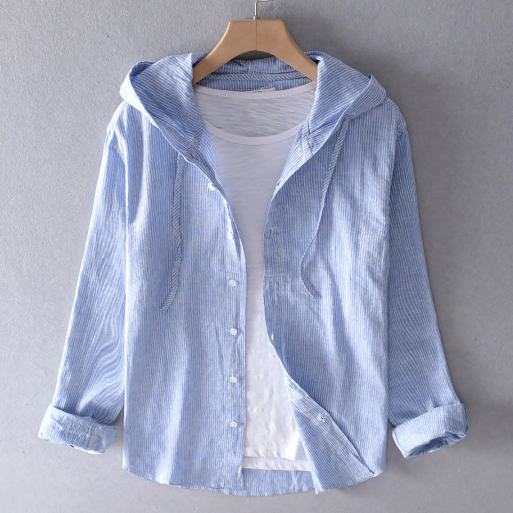 Blouse à capuche rayée bleu clair, boutonnée, manches longues retroussées, portée sur cintre avec un t-shirt blanc en dessous.