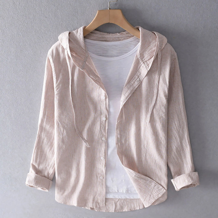 Blouse à capuche beige à fines rayures, boutonnée, manches longues retroussées, présentée sur cintre avec un t-shirt blanc en dessous.