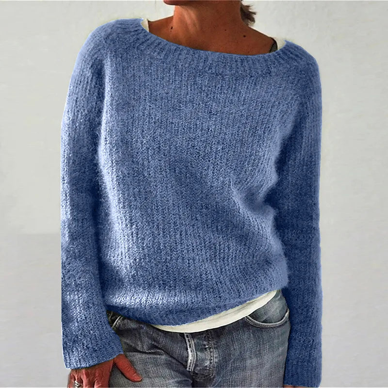 Femme portant un pull en maille bleu clair à coupe décontractée, avec manches longues et encolure large, assorti d’un t-shirt clair et d’un jean, photographiée sur un fond neutre.