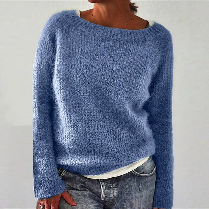 Femme portant un pull en maille bleu clair à coupe décontractée, avec manches longues et encolure large, assorti d’un t-shirt clair et d’un jean, photographiée sur un fond neutre.