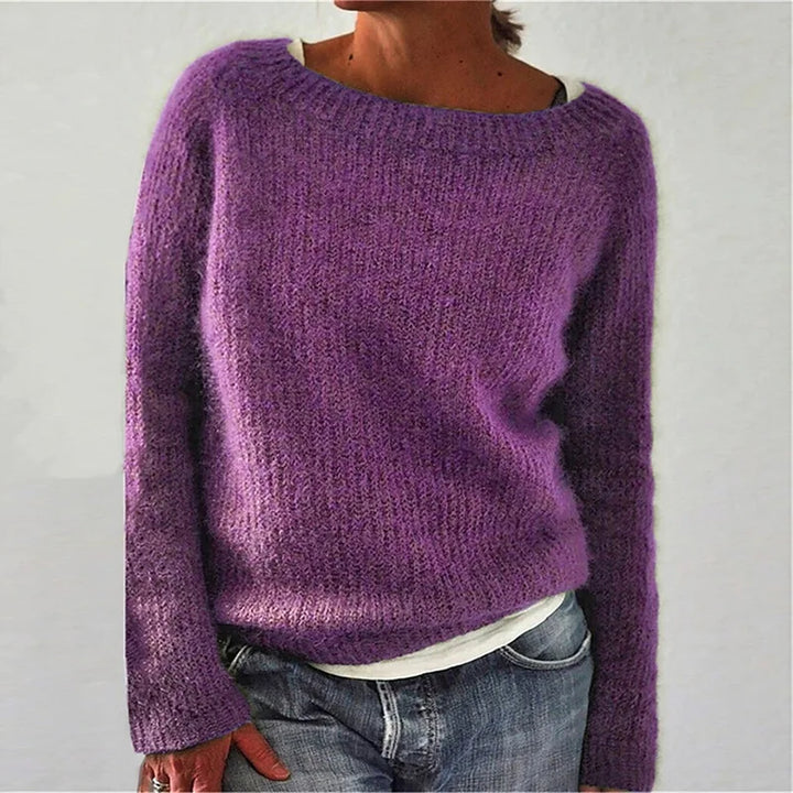 Femme portant un pull en maille violet à coupe décontractée, doté de manches longues et d’une encolure large, associé à un t-shirt clair et un jean, photographiée sur un fond neutre.
