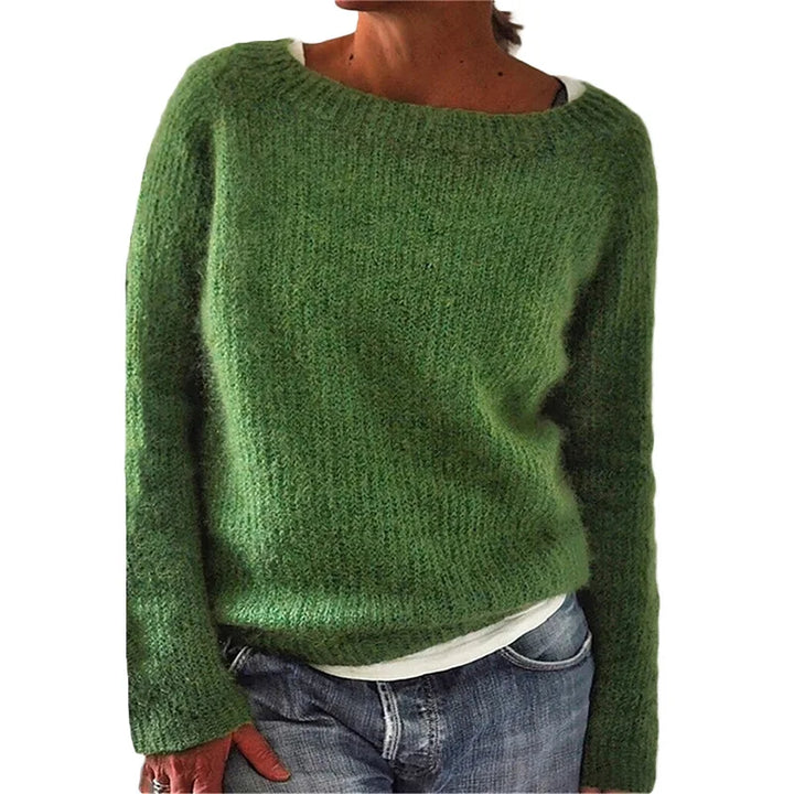 Femme portant un pull en maille vert à coupe décontractée, avec manches longues et encolure large, associé à un t-shirt clair et un jean, photographiée sur un fond blanc.