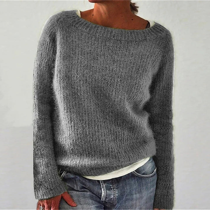 Femme portant un pull en maille gris à coupe décontractée, avec manches longues et encolure large, assorti d’un t-shirt clair et d’un jean, photographiée sur un fond neutre.