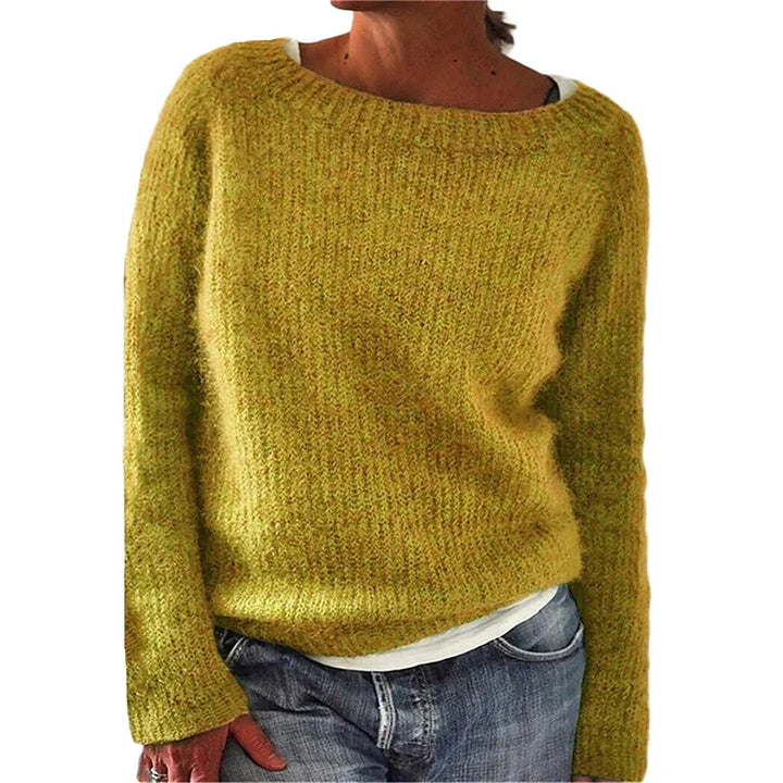 Femme portant un pull en maille jaune moutarde à coupe décontractée, avec manches longues et encolure large, associé à un t-shirt clair et un jean, photographiée sur un fond blanc.