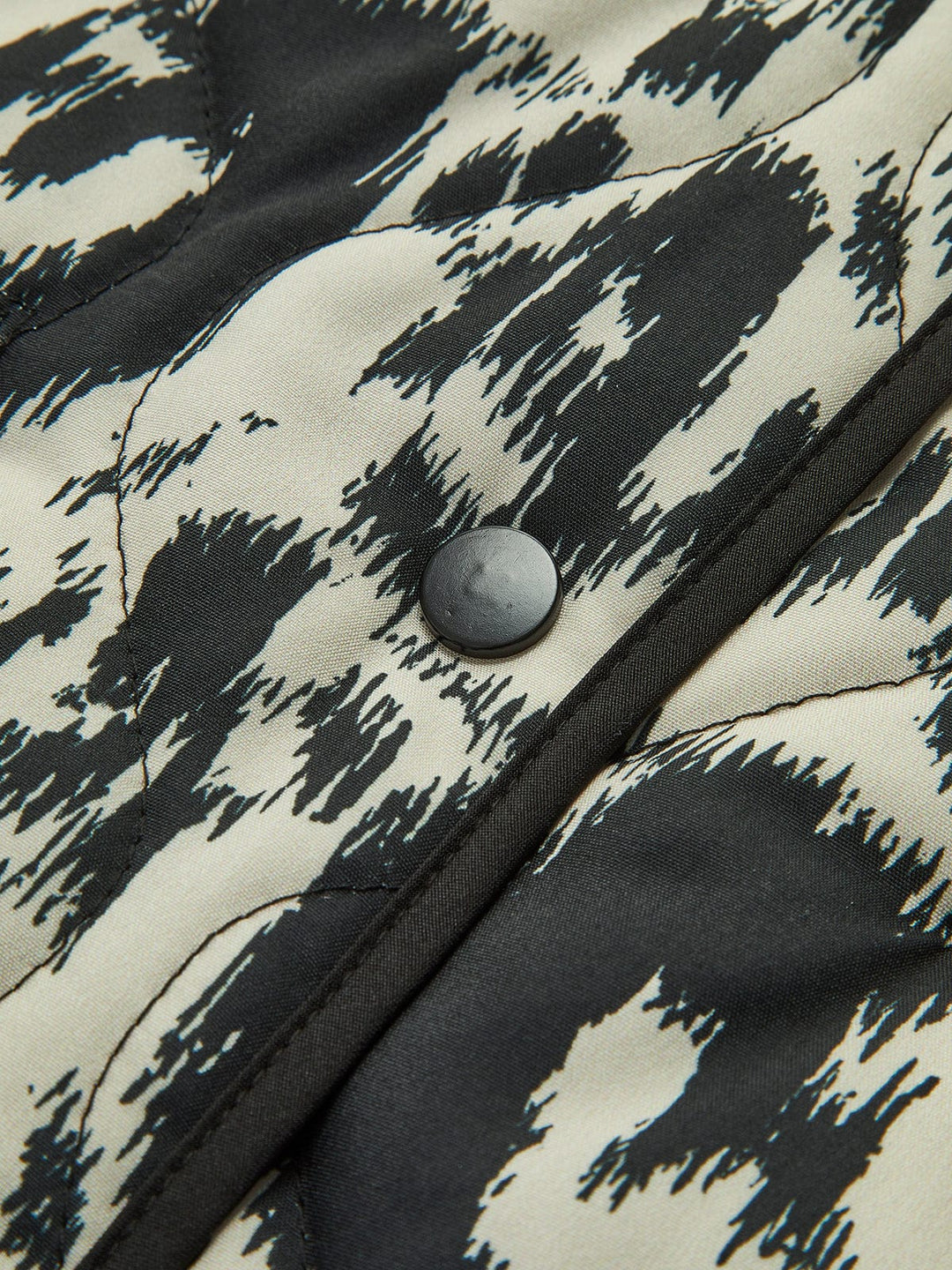 Détail du manteau ajusté à sequins 'Girelle' pour invitées de mariage, mettant en avant le motif animalier noir et blanc ainsi que le bouton noir. Ce manteau moderne présente une finition soignée, avec un design élégant et raffiné qui complète parfaitement une tenue de soirée.