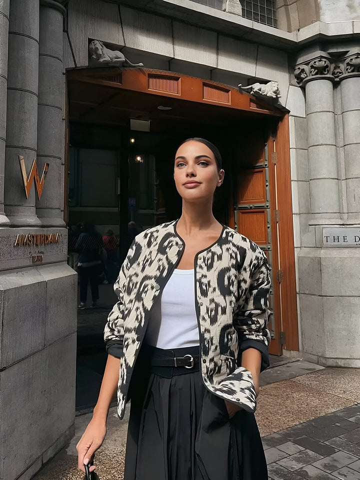 Le manteau ajusté à sequins 'Girelle' pour invitées de mariage porté par une modèle, avec un design moderne et élégant. Le motif animalier noir et blanc s'associe à une coupe ajustée, créant une silhouette raffinée et tendance, parfaite pour des occasions spéciales. Le manteau est porté avec une jupe fluide et une ceinture, apportant une touche chic au look.