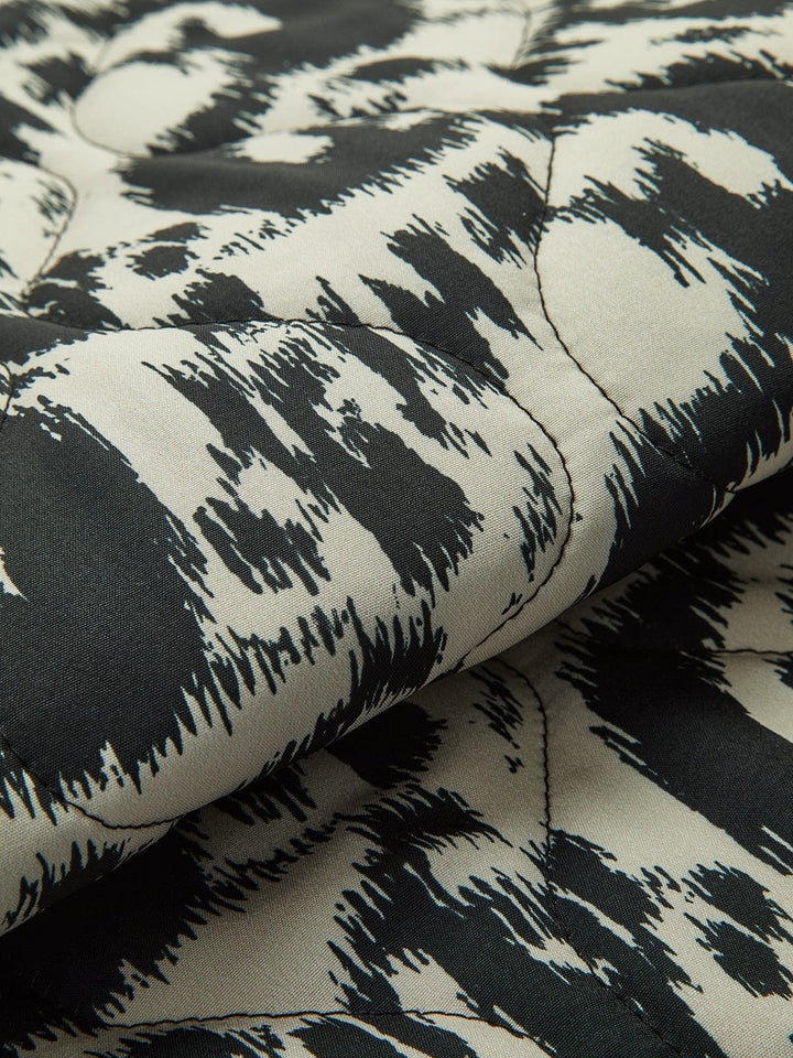 Détail du tissu du manteau ajusté à sequins 'Girelle' pour invitées de mariage, mettant en valeur le motif animalier noir et blanc. Ce zoom sur le tissu montre la texture élégante et la finition soignée, offrant un aperçu du confort et du style moderne du manteau.