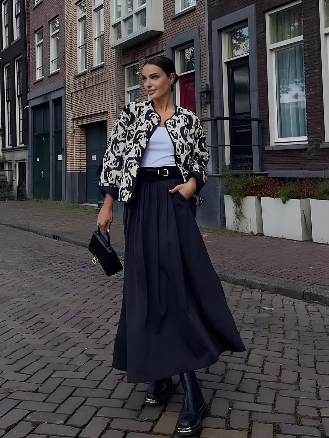Le manteau ajusté à sequins 'Girelle' pour invitées de mariage porté par un modèle dans une rue élégante. Avec son motif animalier noir et blanc, ce manteau moderne s'associe à une jupe longue fluide et des bottes, créant un look chic et raffiné pour toute occasion spéciale.