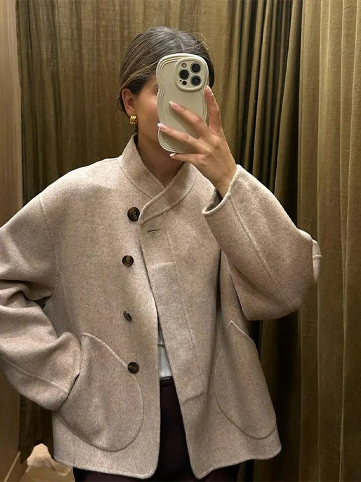 Veste courte pour femme en laine douce et chaude, idéale pour l'hiver. Avec ses boutons en bois et ses poches arrondies, cette veste au design épuré offre un look chic et élégant. Parfaite pour les journées froides, elle se porte facilement sur un pull ou une blouse, apportant confort et style à votre tenue hivernale.