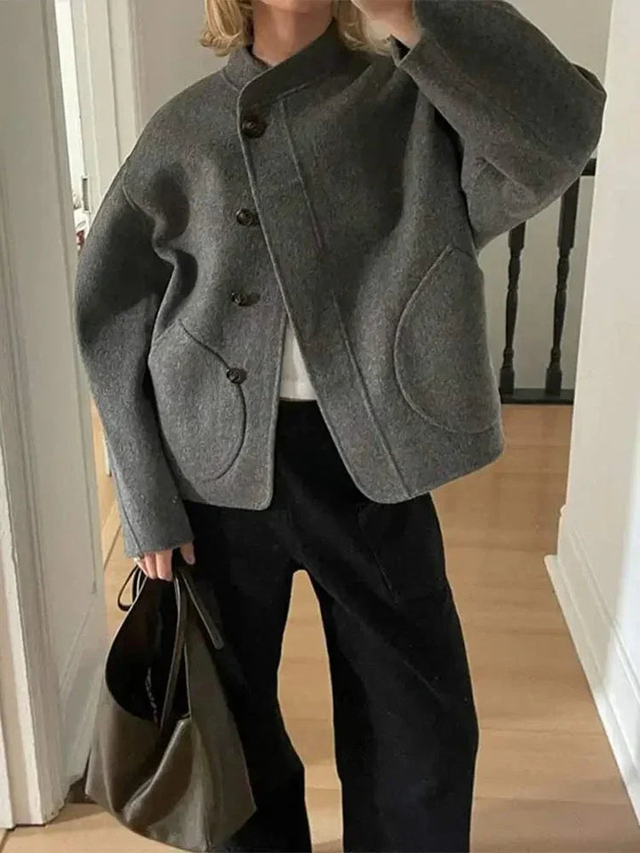 Veste courte en laine grise pour femme, parfaite pour l'hiver. Son design épuré avec des boutons en bois et des poches arrondies lui donne un style moderne et élégant. Elle s'associe facilement avec des pantalons larges ou un jean pour un look chic et décontracté tout en offrant chaleur et confort pendant les mois froids.