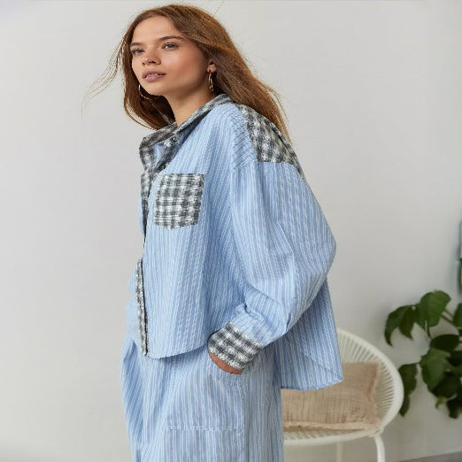 Pyjama pour femme au style moderne, avec chemise ample à manches longues et pantalon coordonné, en tissu bleu clair à rayures fines et empiècements à carreaux, porté pour un look confortable et élégant à la maison.