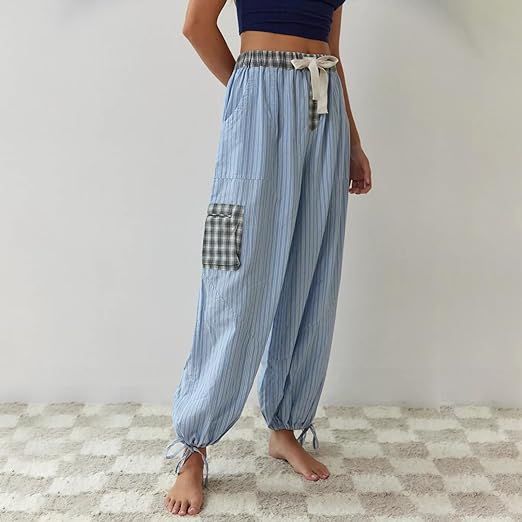 Pantalon de pyjama pour femme à coupe fluide, en tissu bleu clair à rayures fines, avec taille élastique et lien à nouer, poches pratiques et bas resserrés, porté pieds nus pour un confort optimal à la maison.