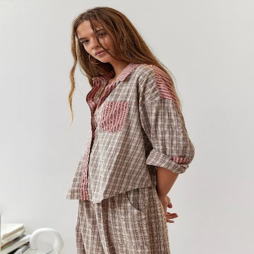 Haut de pyjama pour femme vu de profil, à coupe fluide avec manches retroussées, en tissu à rayures texturées dans des tons beige et rose, avec col ouvert et poche poitrine contrastante pour un style confortable et moderne à la maison.