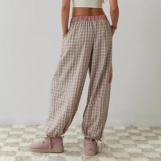 Pantalon de pyjama pour femme vu de dos, à coupe ample, en tissu à carreaux dans des tons beige et rose, avec taille élastique contrastante et bas resserrés par liens, porté avec des bottines pour un style cosy et tendance.