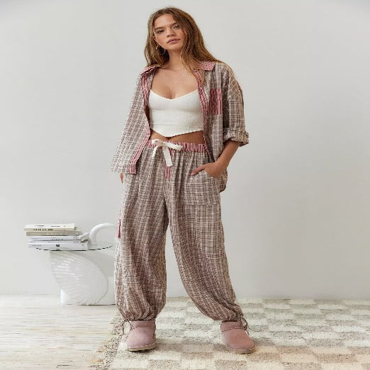 Ensemble de pyjama pour femme porté de face, composé d’un haut ample ouvert et d’un pantalon à coupe fluide, en tissu à carreaux beige et rose avec détails contrastants, porté avec un débardeur blanc pour un style décontracté et tendance à la maison.