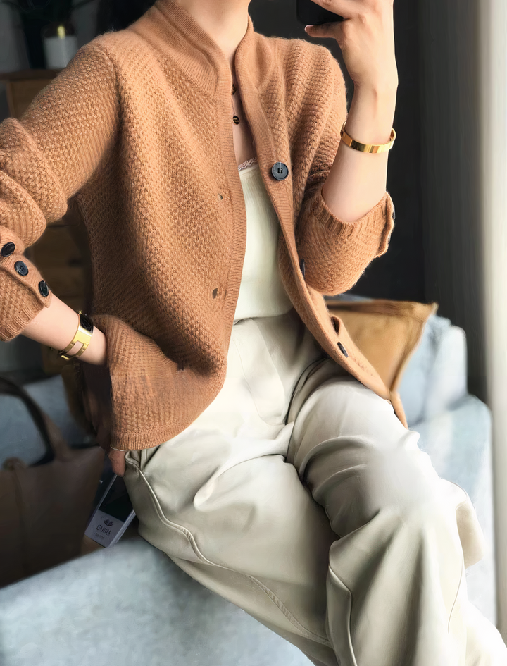 Femme portant un cardigan texturé coloris caramel, doté de boutons sombres et d’un col montant moderne, associé à un débardeur clair et un pantalon beige pour un look chic et décontracté.