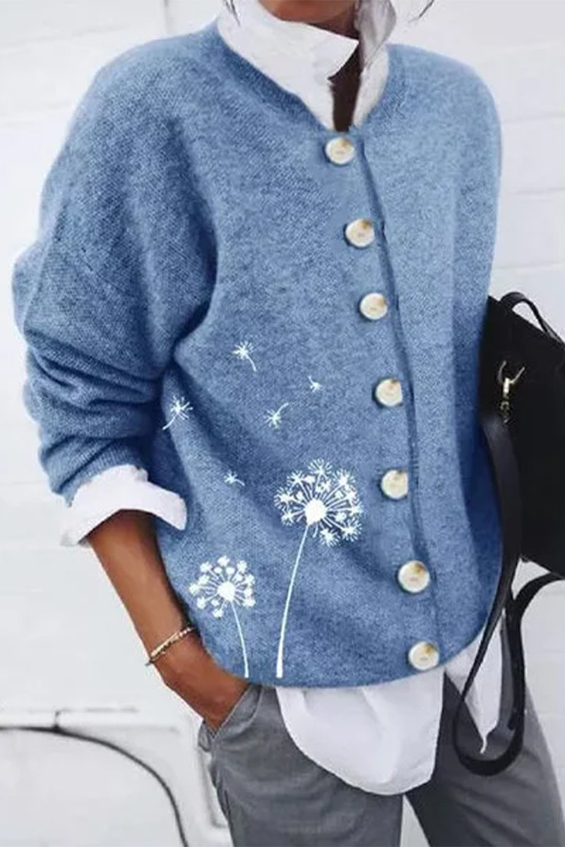 Femme portant un cardigan bleu à boutons nacrés, orné d’un imprimé pissenlit délicat sur le côté, associé à une chemise blanche et un pantalon gris pour un look moderne, frais et décontracté.