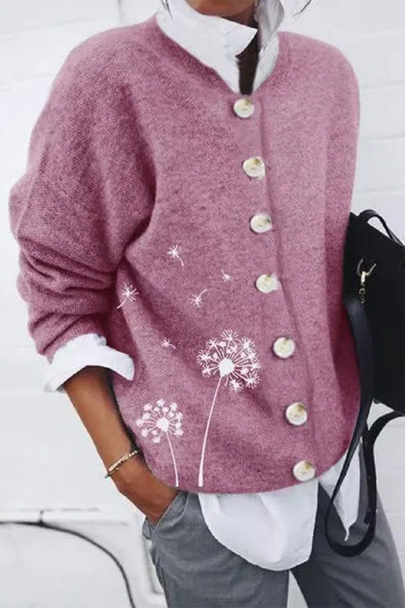 Femme portant un cardigan rose à boutons nacrés, orné d’un imprimé pissenlit délicat sur le côté, associé à une chemise blanche et un pantalon gris pour un look moderne, doux et décontracté.