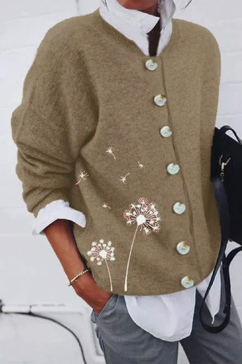 Une femme porte un cardigan marron à boutons de nacre, orné d'un délicat imprimé de pissenlits sur le côté, associé à une chemise blanche et un pantalon gris pour un look moderne et décontracté.