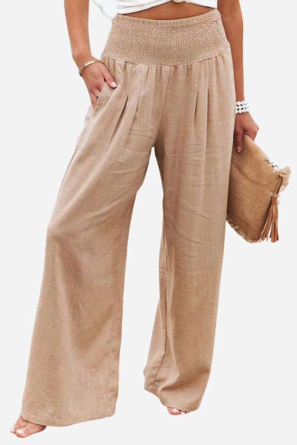 Pantalon palazzo pour femme beige clair, taille haute avec ceinture smockée, coupe très large et fluide en tissu léger, porté avec un haut clair et une pochette pour un style élégant, naturel et estival.