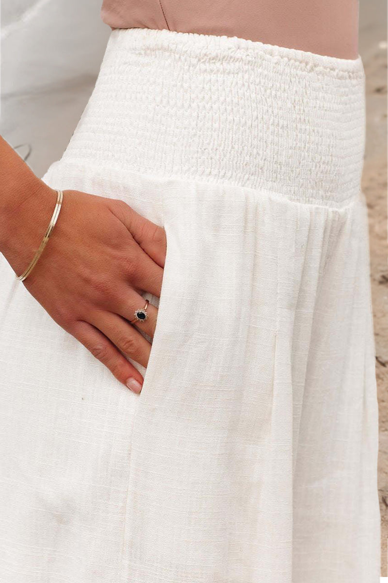 Détail de la taille haute smockée et de la poche latérale d’un pantalon fluide blanc, mettant en avant la finition soignée, le confort et la légèreté du tissu.