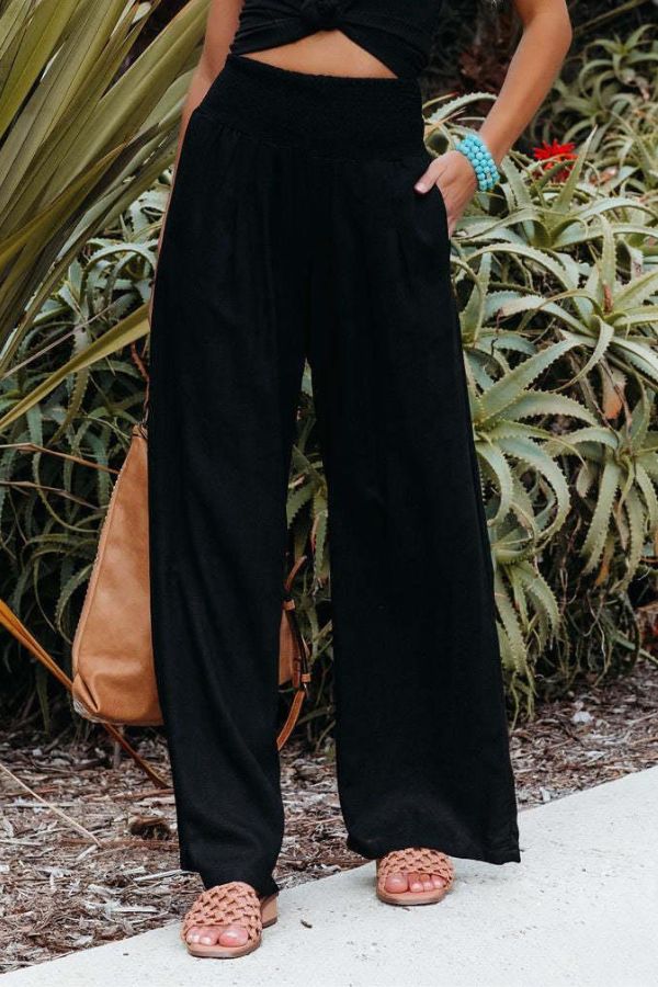 Pantalon palazzo pour femme noir, taille haute et coupe très large, confectionné en tissu fluide, porté avec un haut court et des sandales pour un look chic, moderne et décontracté.