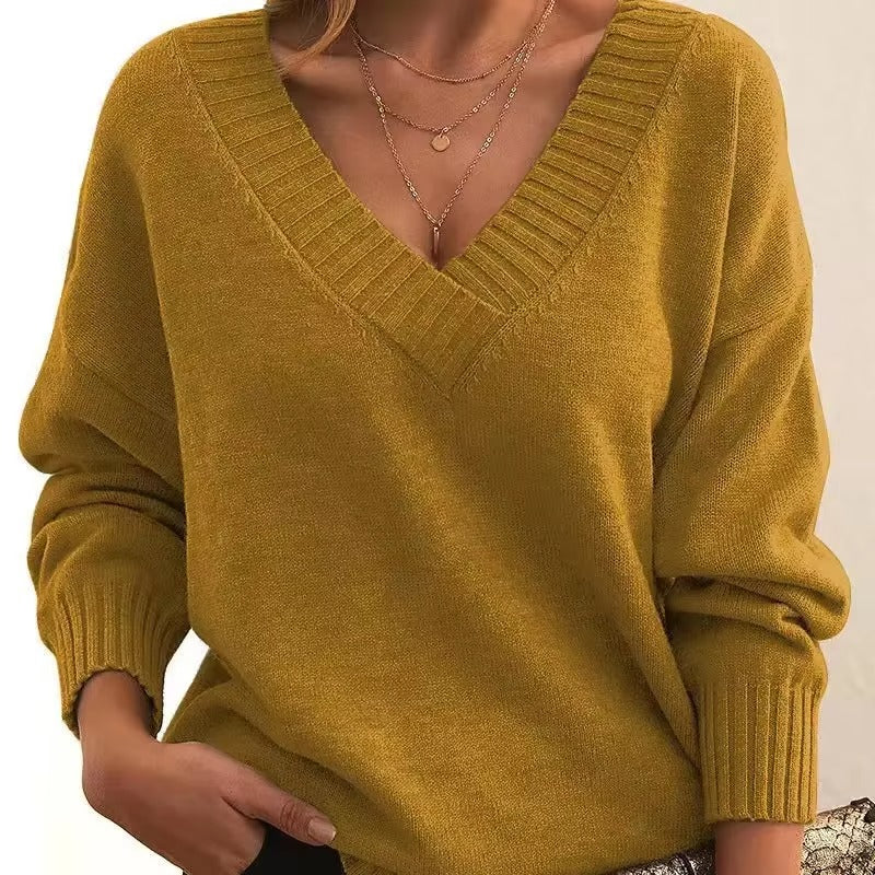 Femme portant un pull en maille jaune moutarde à col en V avec bords côtelés. Les manches sont longues et légèrement amples, et elle porte plusieurs colliers délicats en or. Le look est moderne, chaleureux et décontracté, avec une touche de féminité et de confort.