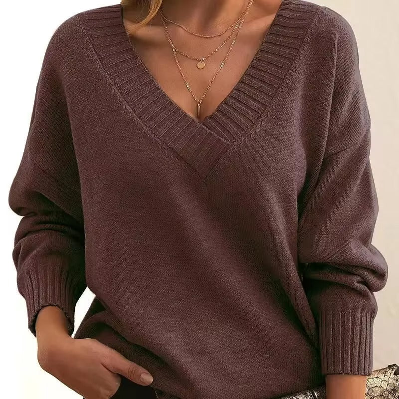 Une femme porte un pull en maille marron à col V et bords-côtes. Les manches longues sont légèrement amples et elle arbore plusieurs colliers en or délicats. Ce look élégant et moderne allie confort et féminité, idéal pour une tenue à la fois décontractée et sophistiquée.