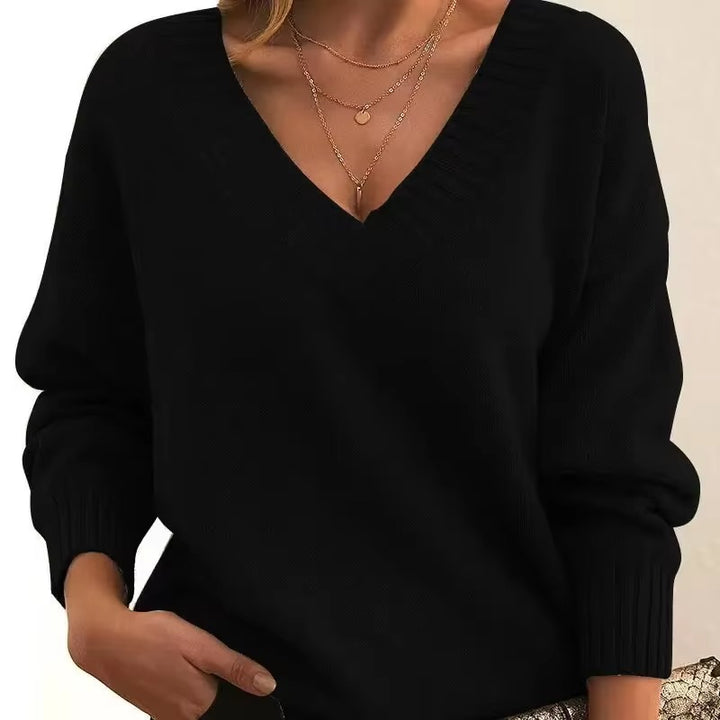 Femme portant un pull en maille noir à col en V avec bords côtelés. Les manches longues sont légèrement amples, et elle porte plusieurs colliers fins en or. Ce look chic et moderne est à la fois élégant et confortable, avec une touche de féminité.