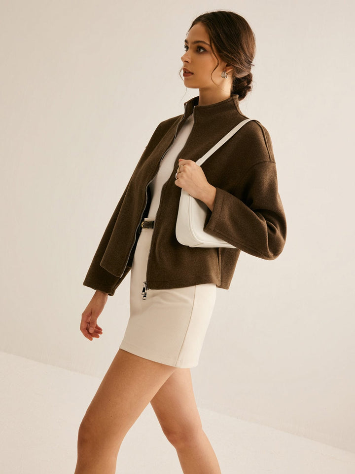 Femme marchant avec élégance, portant un manteau court marron à col montant, une robe blanche et un sac à main blanc, créant un look moderne et raffiné.