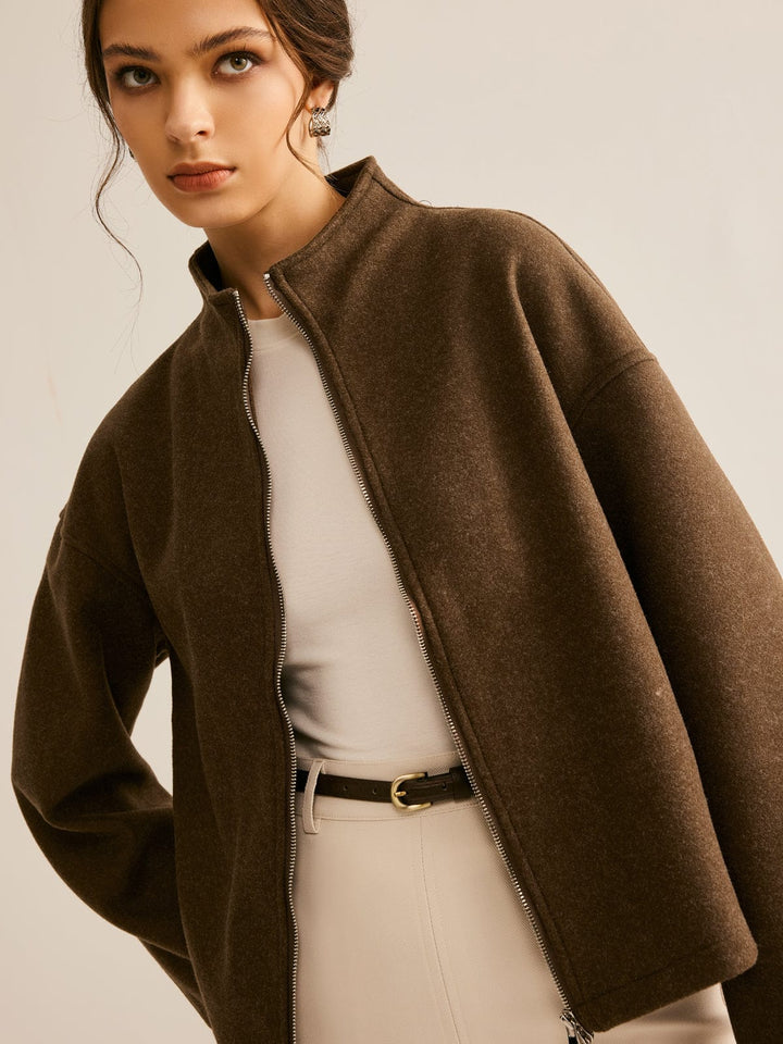 Femme portant un manteau court marron à col montant, avec une fermeture zippée, associé à une robe beige et une ceinture, créant un look chic et moderne.
