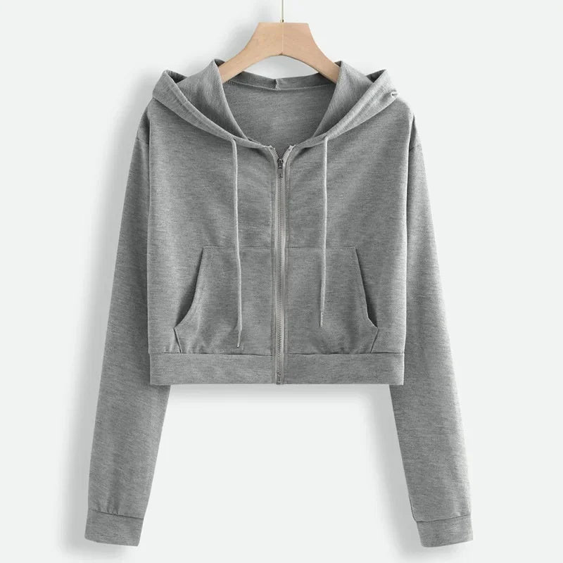 Un sweat à capuche gris clair avec une fermeture éclair sur le devant. Le modèle est court, avec des manches longues et deux poches sur le devant. Il offre un look décontracté et pratique pour une tenue confortable.