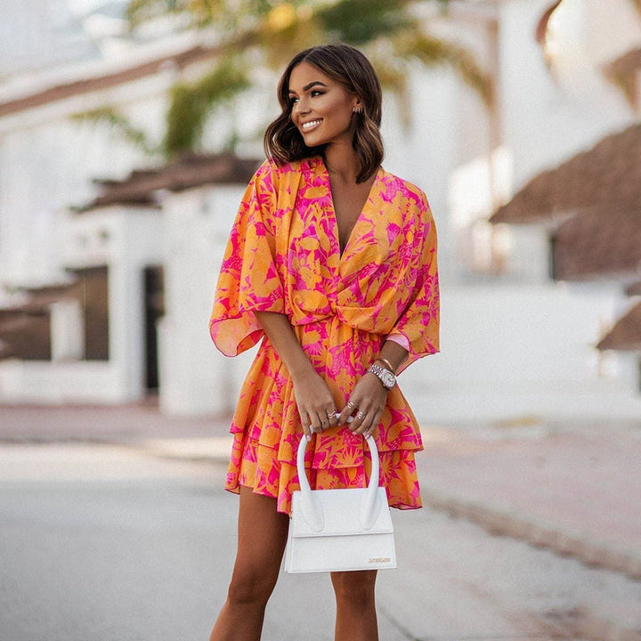 Robe courte colorée aux imprimés floraux vibrants, avec des volants et des manches amples, parfaite pour un look estival audacieux et féminin.