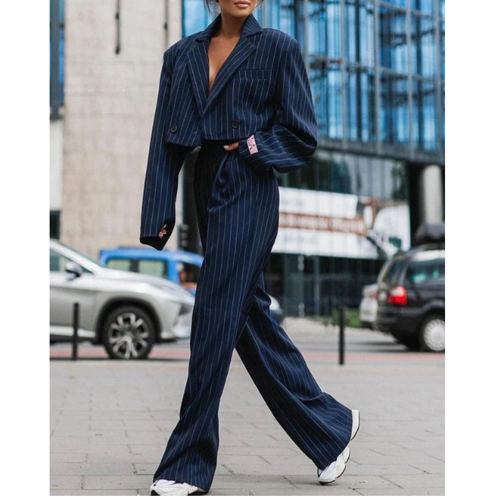 Femme portant le costume formel moderne Isolde blazer oversize bleu marine à fines rayures, pantalon taille haute évasé assorti, look élégant et contemporain en ville.