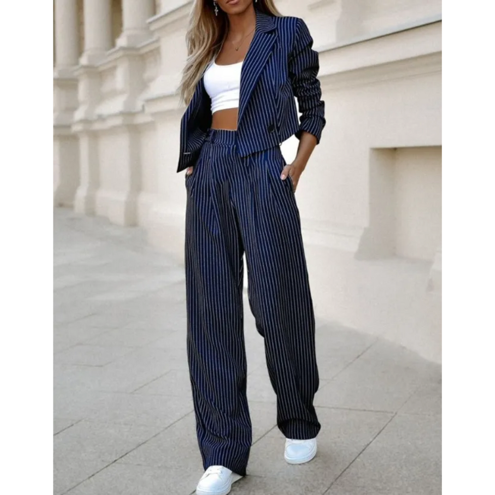 Femme portant le costume formel moderne Isolde blazer court bleu marine à fines rayures avec manches froncées, pantalon large taille haute assorti, style chic et tendance avec top blanc et baskets.