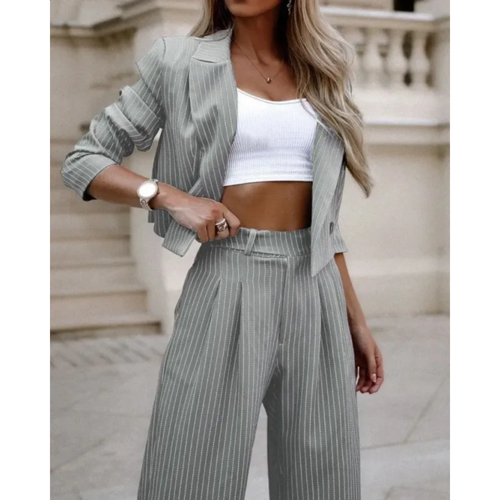 Femme portant le costume formel moderne Isolde blazer court gris clair à fines rayures avec manches retroussées, pantalon large taille haute assorti, look élégant et contemporain avec top blanc.