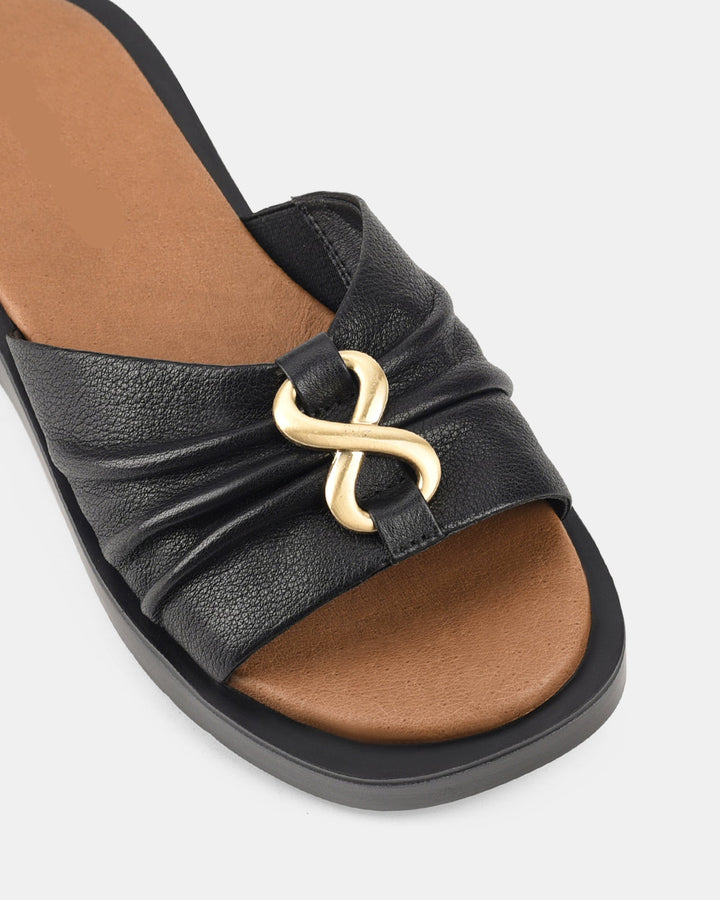 Zoom sur le détail des sandales noires pour femmes, modèle Ivoiry. La coupe élégante avec un jeu de plis sur le dessus et une boucle dorée distinctive ajoutent une touche moderne et chic à ce modèle à semelle ondulée.