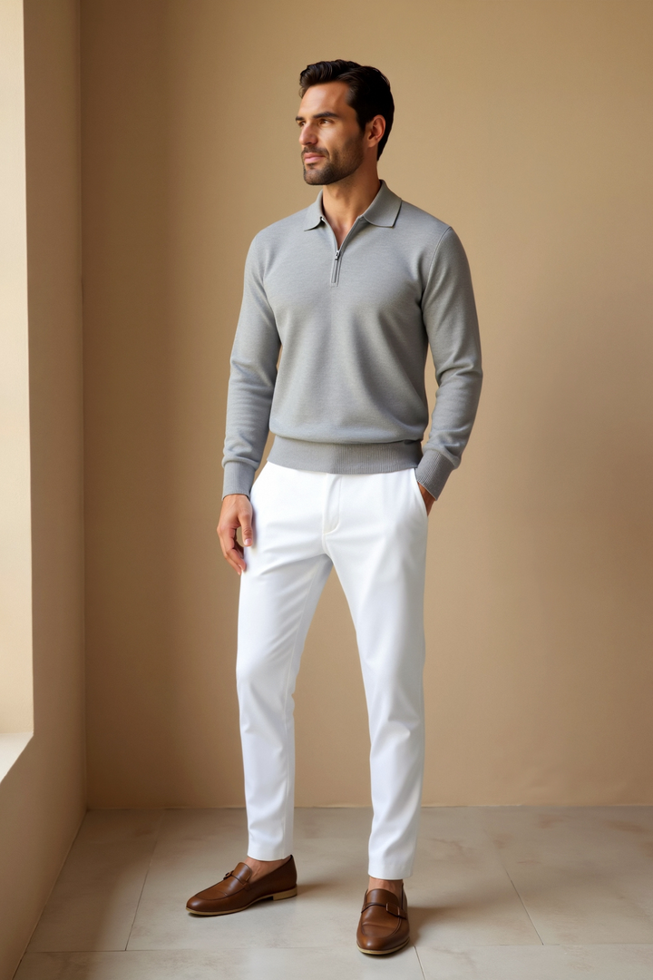 Polo homme zippé tendance gris clair à manches longues, coupe ajustée avec col élégant et fermeture éclair discrète, porté avec un pantalon blanc et des chaussures marron pour un style chic et moderne.