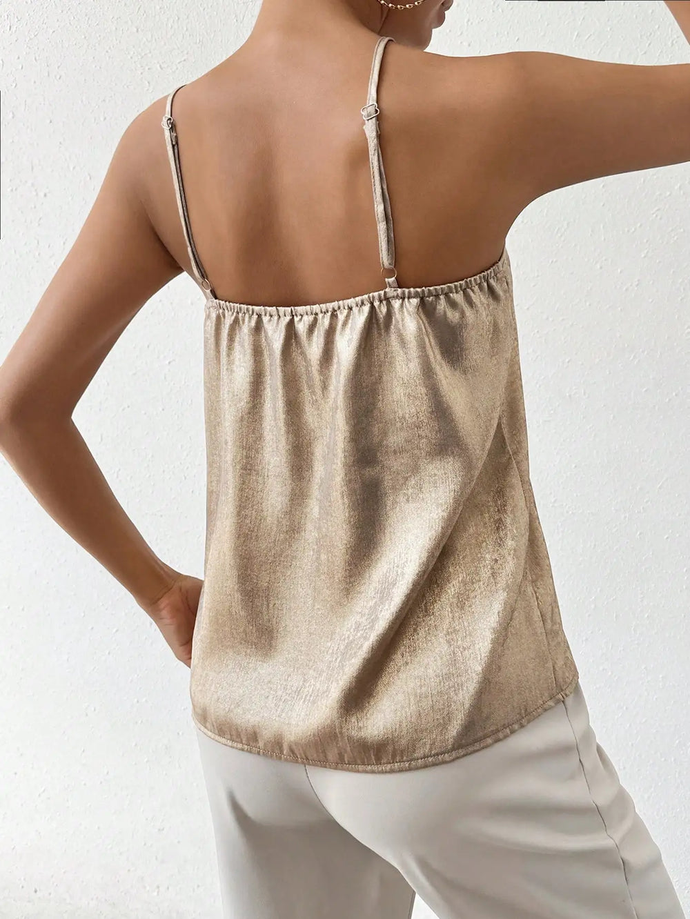 Vue arrière du débardeur doré à fines bretelles et col en V. Le tissu léger et fluide offre un ajustement confortable, parfait pour un look chic et moderne. À associer avec un pantalon blanc pour un style élégant et décontracté.