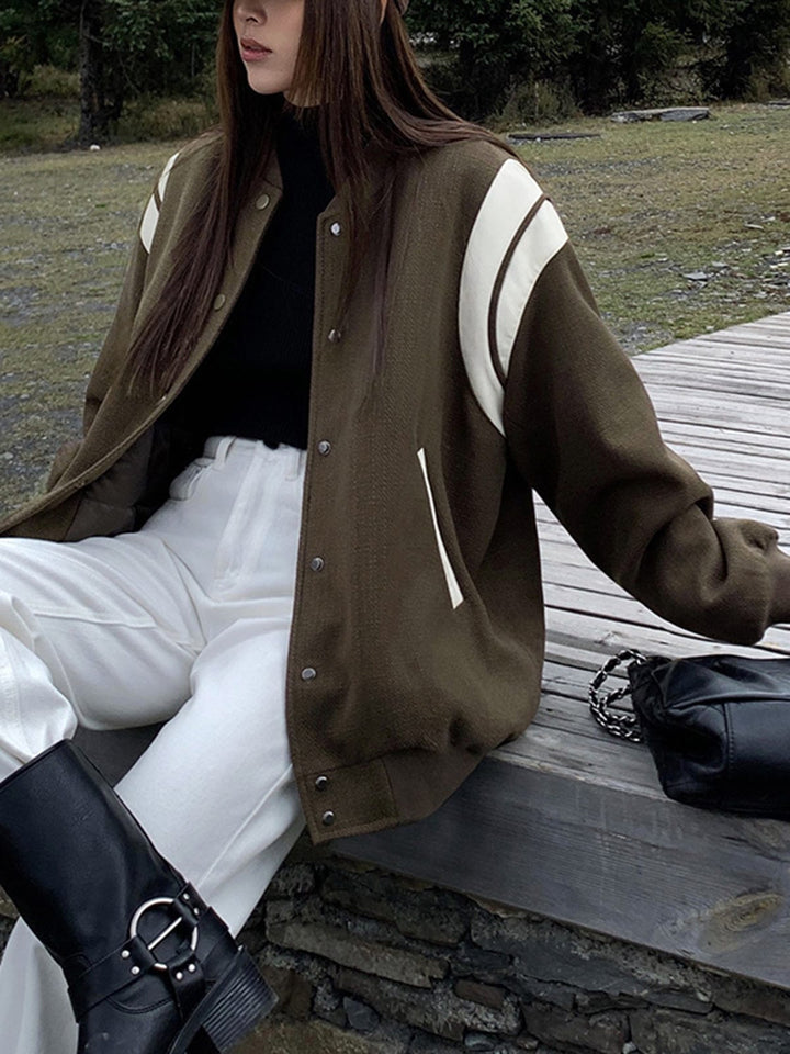 veste kaki olive avec empiècements crème sur les épaules, fermeture par boutons-pression argentés, coupe légèrement oversize; portée avec un pantalon blanc, bottes noires et casquette marron, en pose décontractée en extérieur.