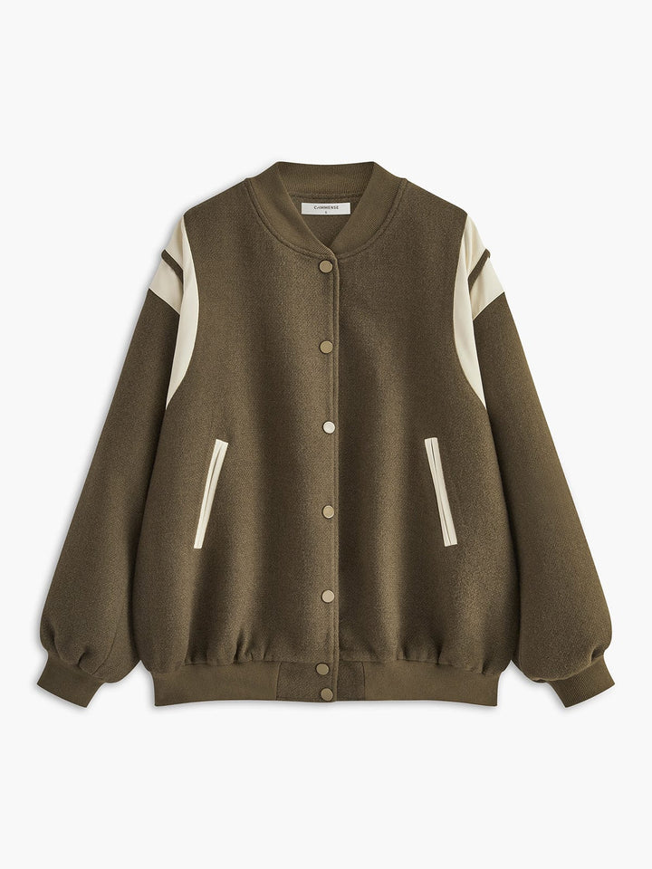 bomber kaki olive avec empiècements crème sur les épaules et les manches, fermeture par boutons-pression et poches latérales, coupe légèrement oversize; sac noir posé sur le banc à ses côtés, tenue décontractée en extérieur.