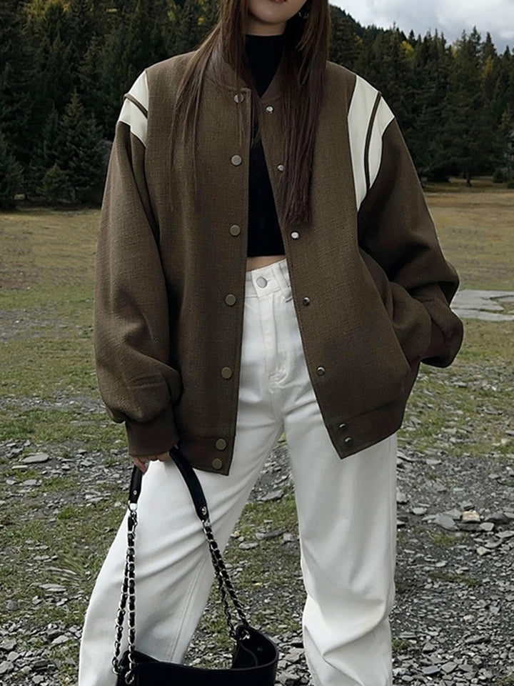 veste bomber kaki olive avec empiècements crème sur les épaules, fermeture par boutons-pression et poches latérales, coupe légèrement oversize; tenue associée à un pantalon blanc et un sac noir, look tendance en extérieur automnal.