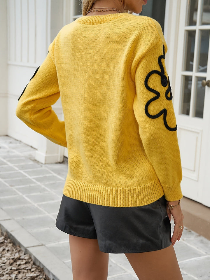 Ce pull jaune vif à manches longues présente des motifs floraux noirs sur les épaules et les manches. Il est associé à un short en simili cuir noir, créant ainsi un look tendance et décontracté parfait pour les journées fraîches.