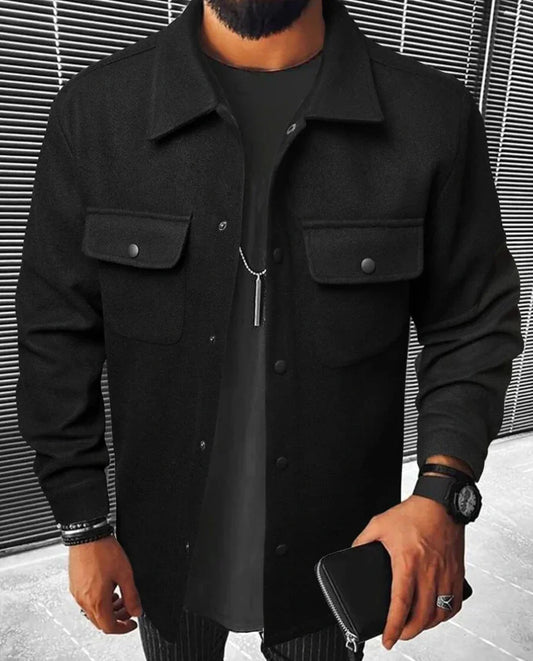 Jules | Chemise oversize noire pour homme à manches longues, avec poches à rabat et boutons noirs, portée sur un t-shirt noir, accessoirisée avec une montre et une pochette.