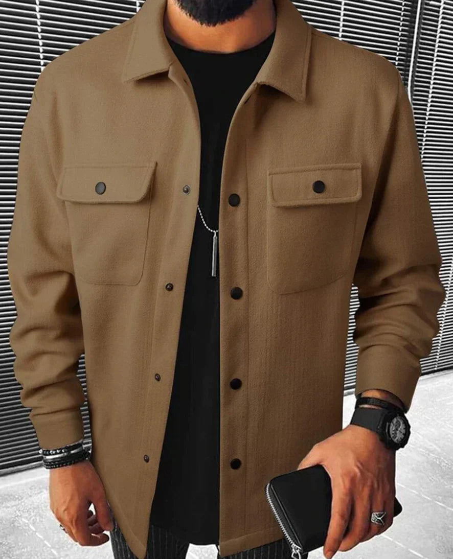 Jules | Chemise oversize pour homme à manches longues, couleur beige, avec poches à rabat et boutons noirs, portée sur un t-shirt noir avec un pantalon à rayures.