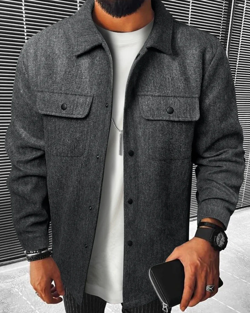 Jules | Chemise oversize pour homme à manches longues, couleur gris foncé, avec poches à rabat et boutons noirs, portée sur un t-shirt blanc et un pantalon à rayures.