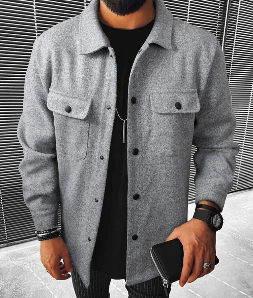 Jules | Chemise oversize pour homme à manches longues, couleur grise, avec poches à rabat et boutons noirs, portée avec un t-shirt noir et un pantalon à rayures.