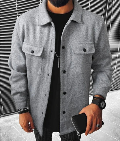 Jules | Chemise oversize pour homme à manches longues, couleur grise, avec poches à rabat et boutons noirs, portée avec un t-shirt noir et un pantalon à rayures.
